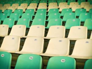 Rows of empty, numbered plastic seats in vibrant green and cream colors at a stadium.