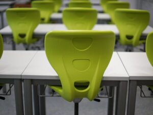 An empty modern classroom featuring rows of vibrant green plastic chairs and white desks.