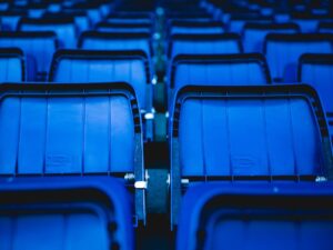 Close-up view of empty blue plastic seats in an outdoor stadium setting.
